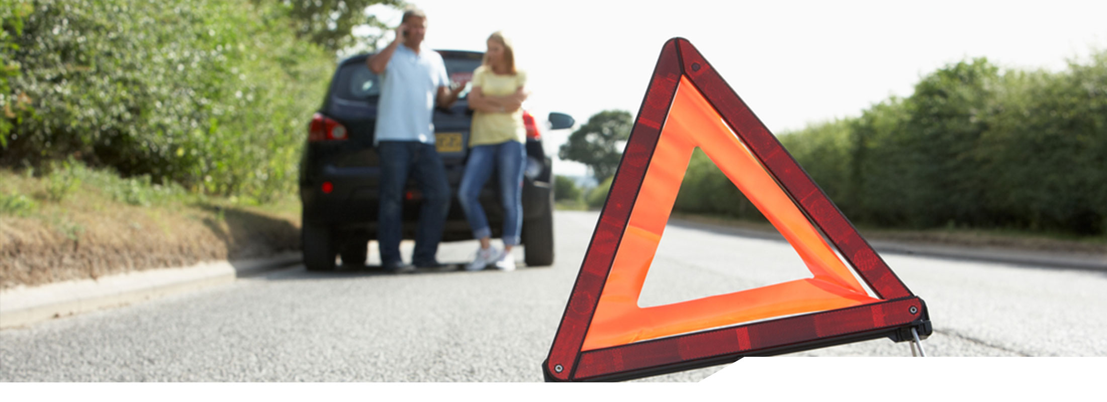 Husband and wife standing next to their vehicle on the side of the road in the background with a hazard sign in the foreground