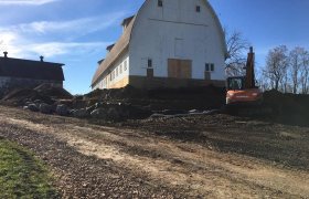 Distance photo of a barn in the background with a feildstone boulder retaining wall being developed around it